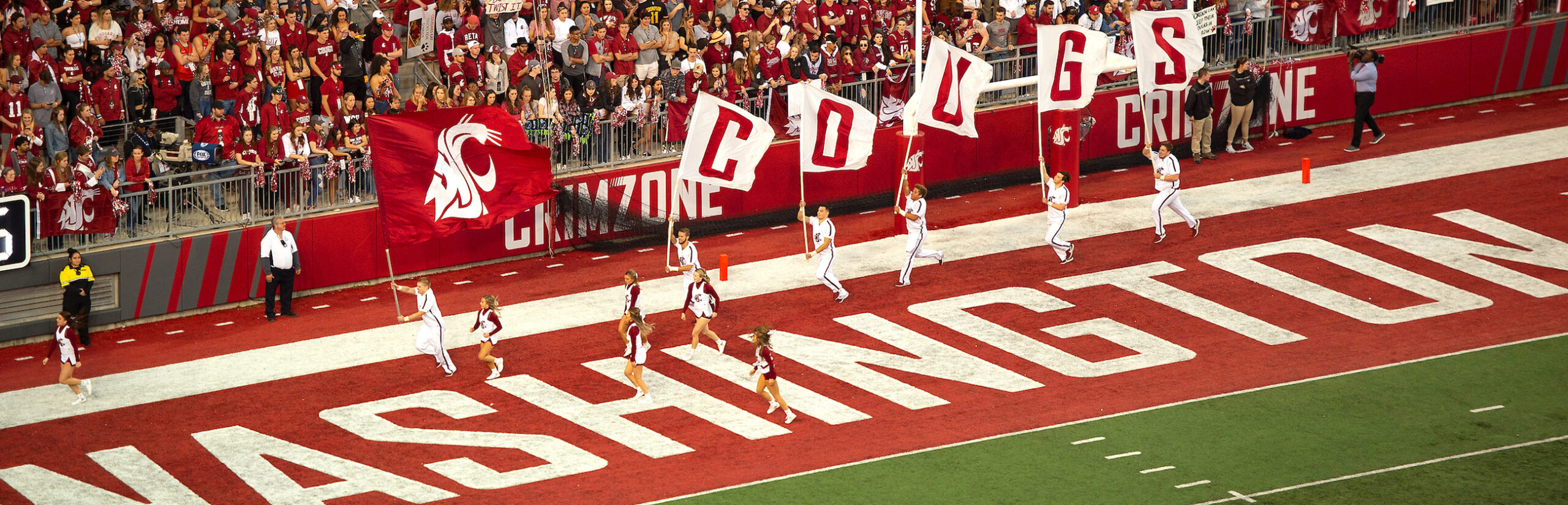 Cheerleaders running with flags that spell Cougs with the WSU logo.