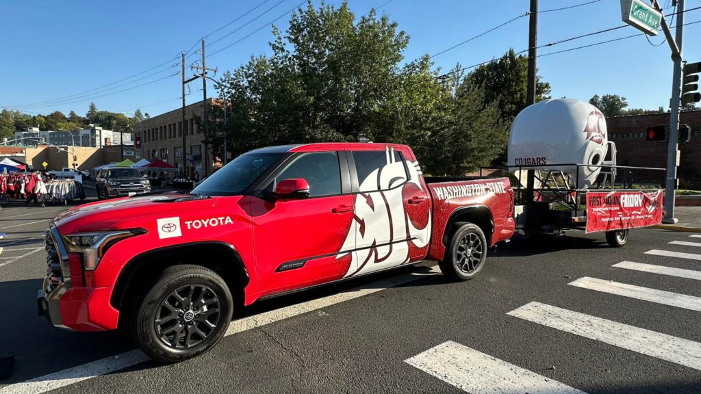 A WSU-branded Toyota pickup truck pulling a trailer with a large sculpture of a Cougar football helmet and a banner advertising First Down Fridays.