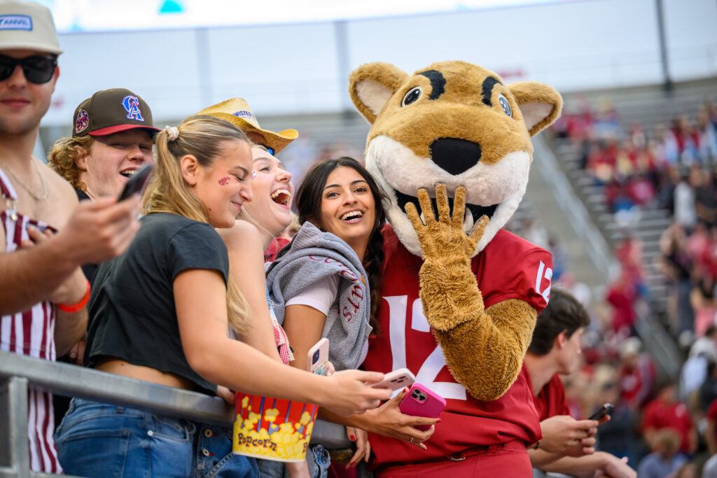 WSU mascot Butch cougar standing with smiling fans in a stadium.