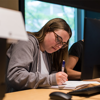 A woman focused on writing notes on a piece of paper, showcasing her concentration and creativity in a serene environment.