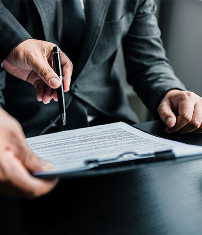 Two individuals in business attire reviewing a document on a clipboard, with one person holding a pen and pointing at the paper.
