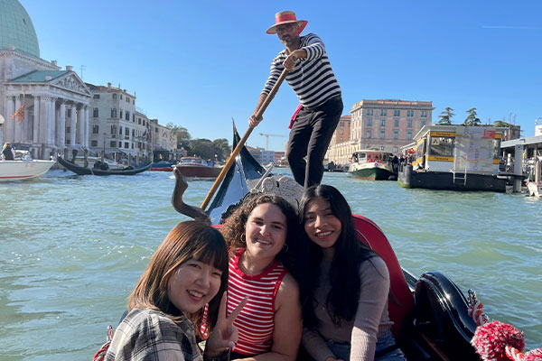 3 women ride a traditional gondola while visiting Venice, Italy