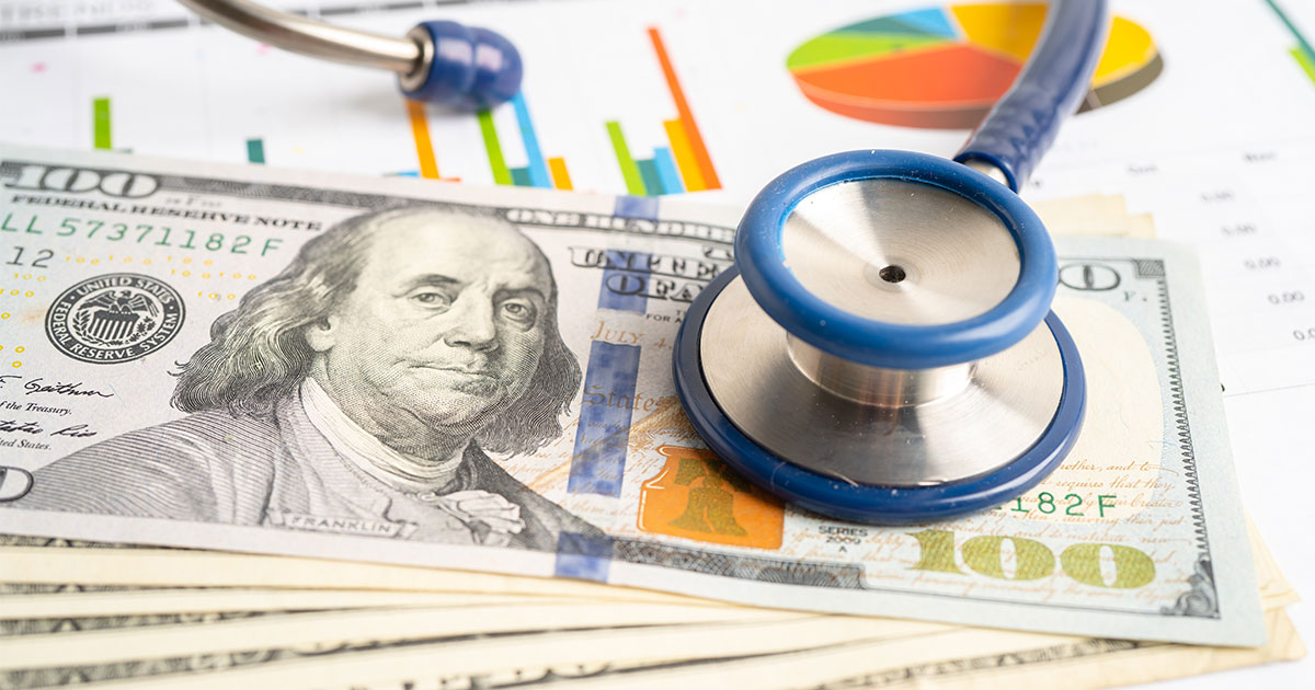A stethoscope lying on a stack of 100-dollar bills, with colorful financial charts and graphs in the background, representing the financial aspects of healthcare.