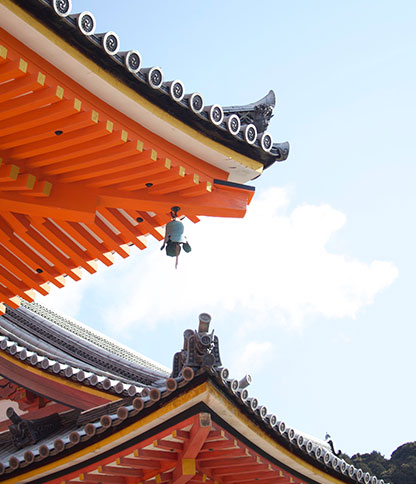 Ornate roof of a traditional Japanese building with vibrant orange and black details under a clear sky.
