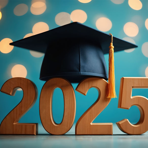 Wooden numbers forming “2025” with a black graduation cap and gold tassel placed on top, set against a blue background with warm bokeh lights.