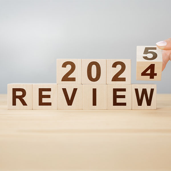 Wooden blocks arranged to display “2024 REVIEW,” with a hand turning the last block to change the 4 into a 5, symbolizing the transition to 2025.