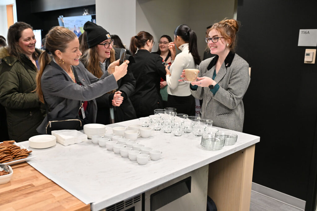Guests gather around a counter with cups, glasses, and plates of cookies during the School of Hospitality Business Management open house showcasing the new beverage lab for wine and beverage business management education.