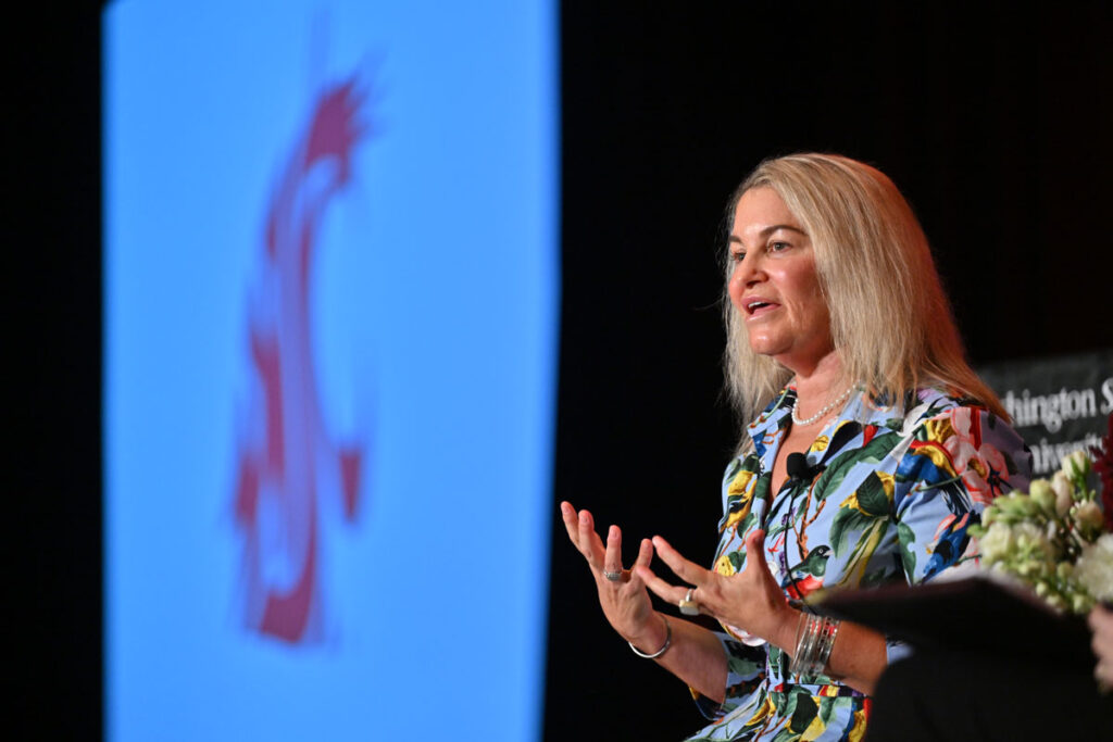 Former Starbucks CFO Rachel Ruggeri speaks on stage at the Washington State University Power Breakfast event, gesturing with hands as a WSU logo is projected in the background.