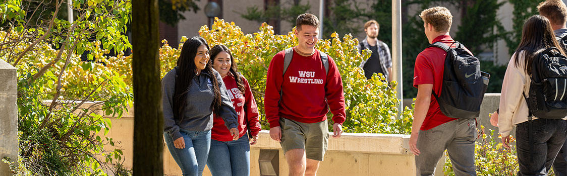 Students walking outdoors on a sunny day, wearing backpacks and WSU apparel.