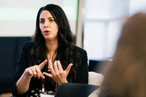 Korey Schramm gesturing with both hands during a discussion in an indoor setting.