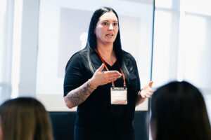 Sarah Collins speaks to an audience, gesturing with both hands during a presentation at the Women in Sales event.