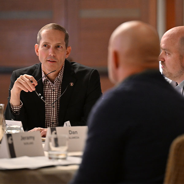 Group seated around a conference table with nameplates visible, engaged in discussion.