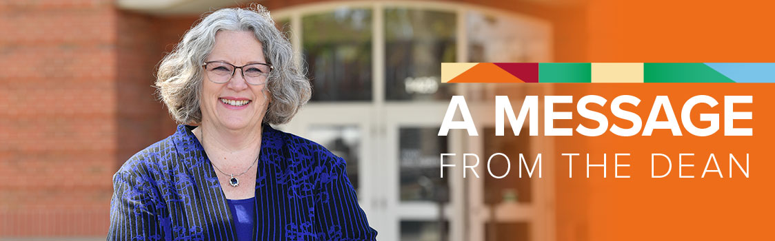 Debbie Compeau standing outdoors in front of a brick building entrance, wearing a patterned blue jacket and necklace. On the right side of the image, an orange banner displays the text “A Message From the Dean” with a colorful geometric accent above the text.