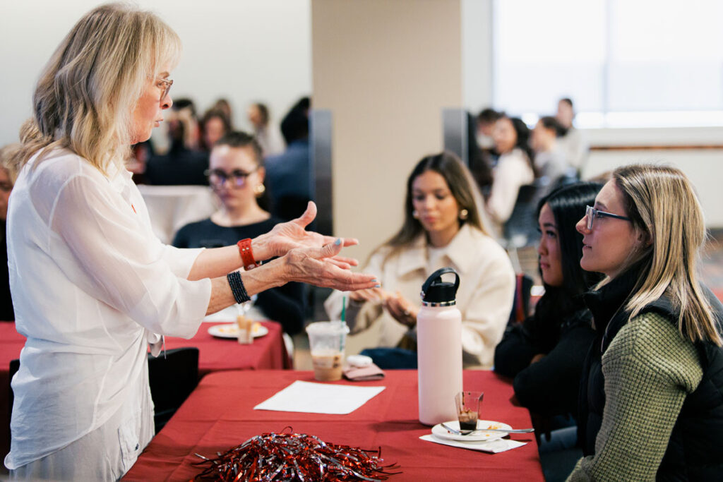 Linda Nihoul speaks to attendees at a table during the 2025 Women in Sales networking event, sharing insights on gender differences in the workplace.