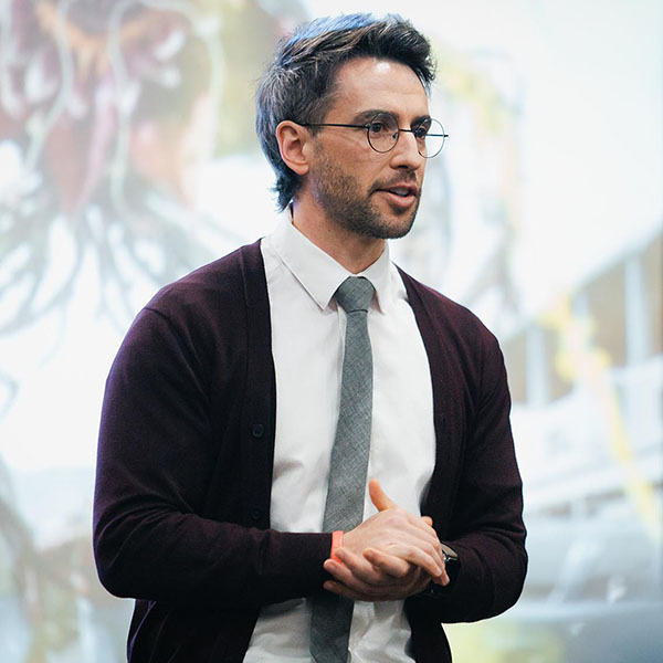 PhD Student Josh Groves in business attire speaking at an event.