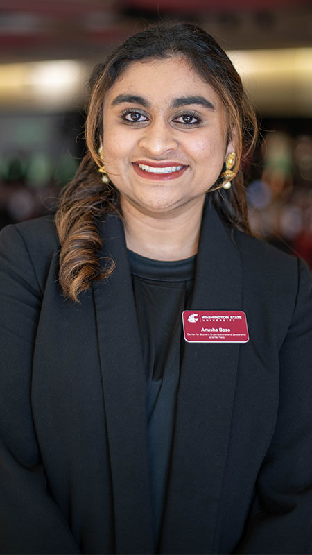 Anusha Bose wearing a black blazer and gold earrings, with a name badge that reads “Anusha Bose” at a professional event.