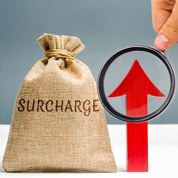 Burlap sack labeled “Surcharge” next to a red upward arrow viewed through a magnifying glass, symbolizing rising costs or fees.