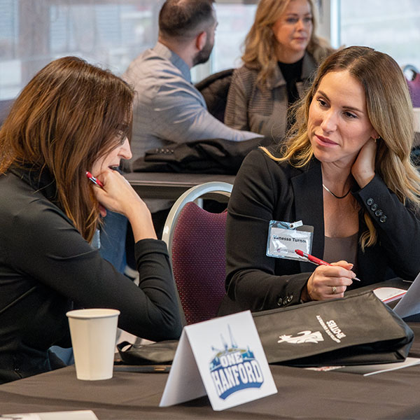Two participants seated at a table during the Tri-Cities One Hanford Leadership Academy, engaged in discussion with notebooks and event materials in front of them.