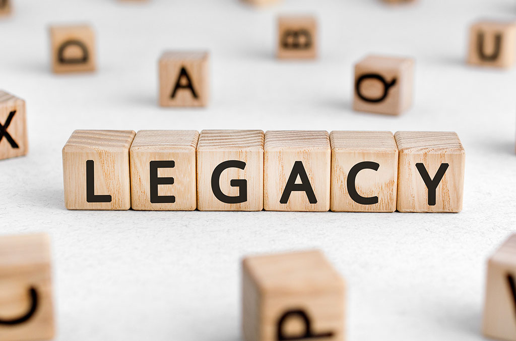 Wooden blocks arranged to spell the word “LEGACY,” with other scattered letter blocks in the background.