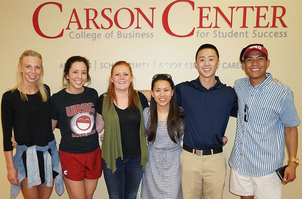 Six people standing side by side in front of a wall sign that reads “Carson Center, College of Business for Student Success,” with additional text mentioning advising, scholarships, study abroad, and careers.