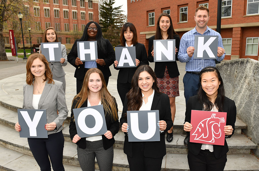 Group of people standing outdoors holding signs that spell “THANK YOU,” with one sign displaying the Washington State University logo.