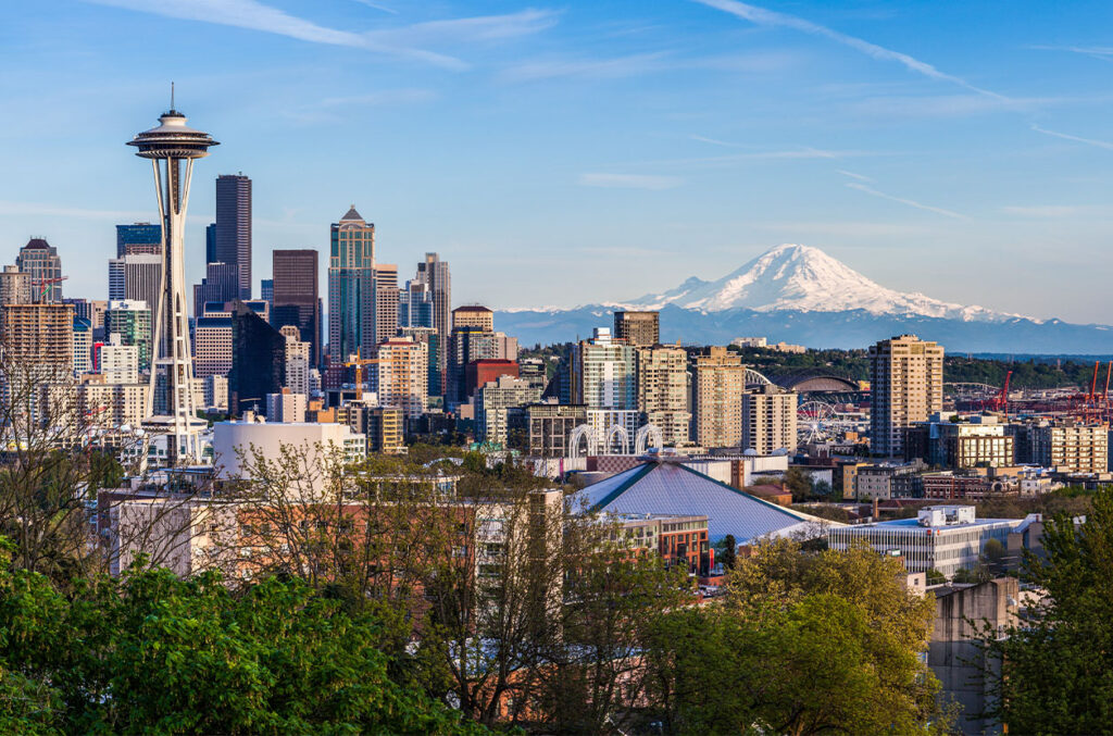 Seattle skyline with the Space Needle and downtown buildings, with Mount Rainier rising in the background under a clear blue sky.