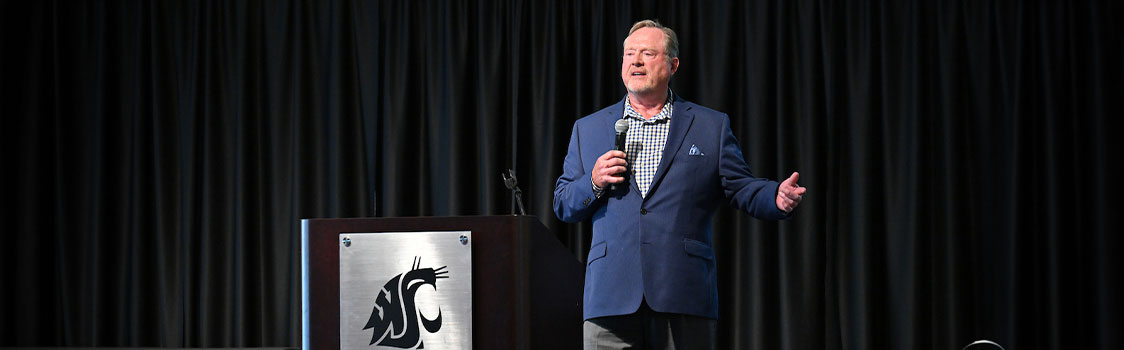 Dan Lynch speaks on stage beside a WSU podium, holding a microphone during an entrepreneurship event.
