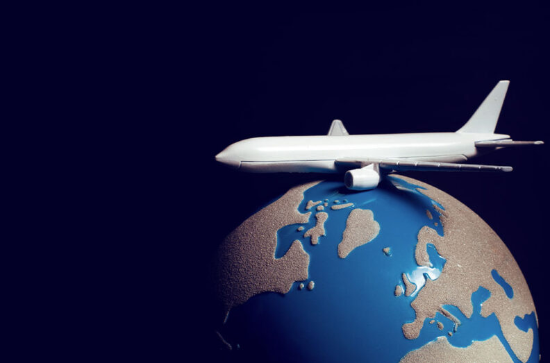 White model airplane rests atop a small blue‑and‑gold globe against a dark background, symbolizing global travel or international business.