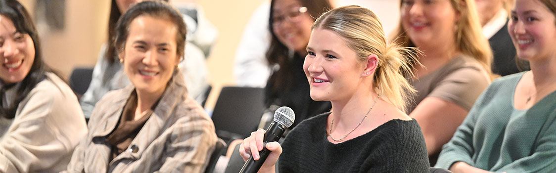 Audience member holding a microphone during a Q&A session at the “Technology for the Business of Aging” event, with other attendees seated in the background.