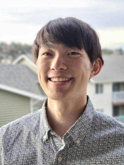 Kakeru Uchiyama standing outdoors in a patterned button‑up shirt, with soft daylight and residential buildings in the blurred background.