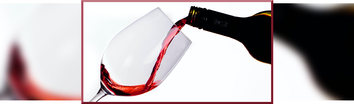 Red wine being poured from a bottle into a tilted wine glass against a white background.