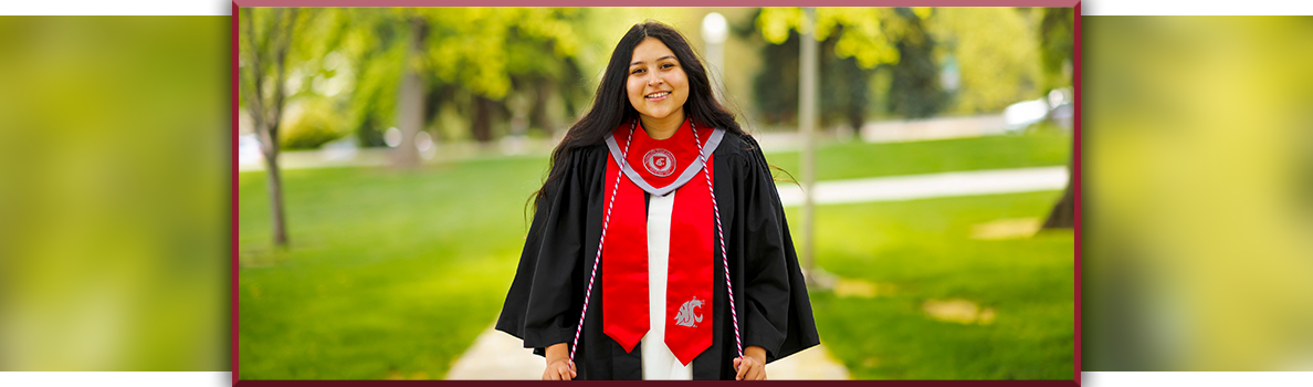 Preciosa Miranda standing on a campus walkway in a black graduation gown with a bright red WSU stole and honor cords, surrounded by green trees and lawn.