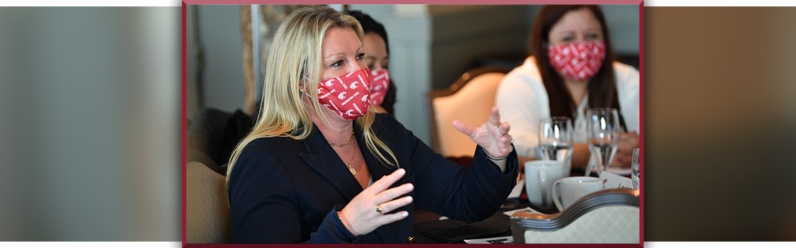 Laura Armstrong speaks and gestures while seated at a table during the Executive MBA Leadership Conference, with glasses and table settings in front of her.