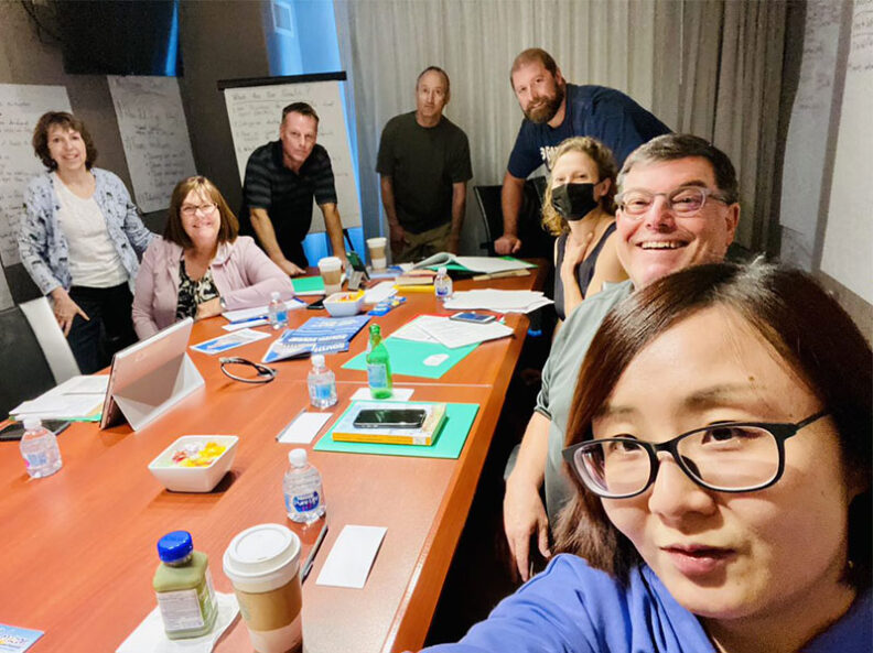 Group seated and standing around a conference table covered with notebooks, drinks, and project materials, including members of the Federal Way tourism project team.