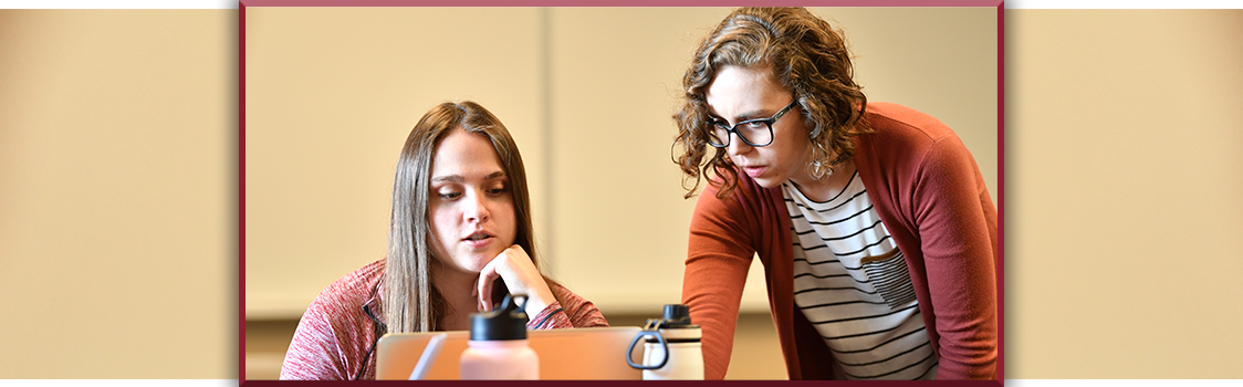 Mycah Harrold works with an undergraduate student during a January 2020 research‑methods class, leaning in to offer guidance at a laptop.