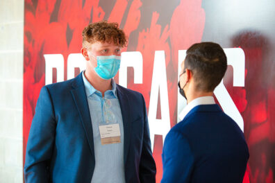 Andrew Parker listens to feedback on his elevator speech while talking with another participant in front of a red "Cougars" backdrop.