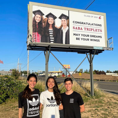 Kathryn, Kristen, and Michael Saba stand together in front of a Vancouver billboard congratulating the Saba triplets on their 2021 graduation.