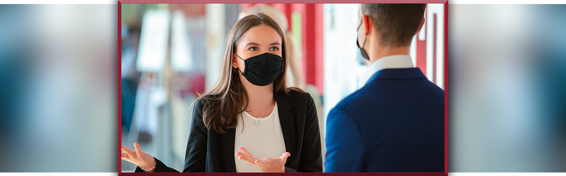 Quincy Thuma practices her elevator speech with Assistant Professor Alec Pappas at the WSU Career Fair, gesturing as they talk in a busy hallway.