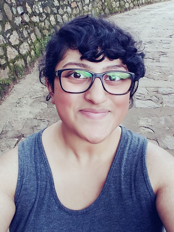 Vinitha Vithayathil outdoors on a stone pathway beside a moss-covered rock wall, wearing a sleeveless gray top.