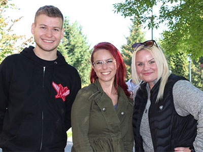 Three Vancouver accounting students, Christian Russ, Jennifer Gragg, and Nicole May—stand outdoors together under leafy trees.