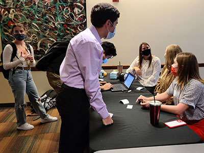 Beta Alpha Psi officers sit at a check‑in table assisting students, with laptops, forms, and supplies arranged across the black tablecloth.