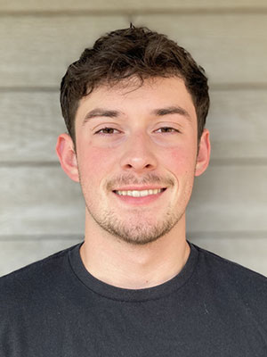 Connor North wearing a dark T‑shirt, standing in front of a light wood‑paneled wall.