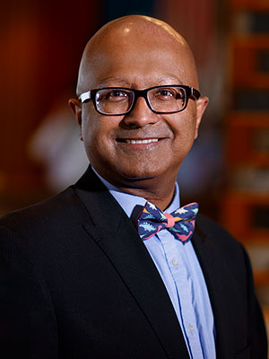 Dipra Jha wearing a dark blazer, light blue shirt, and patterned bow tie, standing indoors with a softly blurred background.