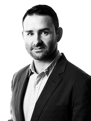 Dustin Winkleman wearing a collared shirt and blazer in a black‑and‑white portrait against a plain background.