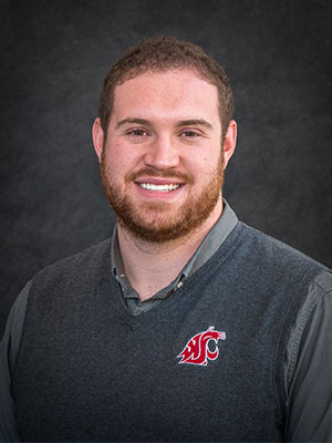 Evan Barton wearing a gray collared shirt and a WSU‑logo vest, posed against a dark textured backdrop.