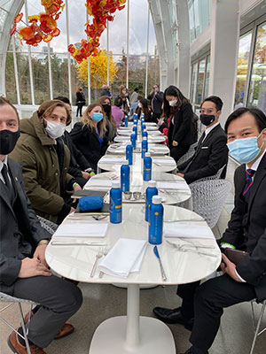 Hospitality Business Management students sit at long, set tables inside a bright glass atrium with hanging glass sculptures during their Seattle industry tour.