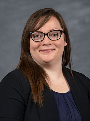 Jacqui LaCroix wearing a navy top and black blazer, posed against a gray studio background.