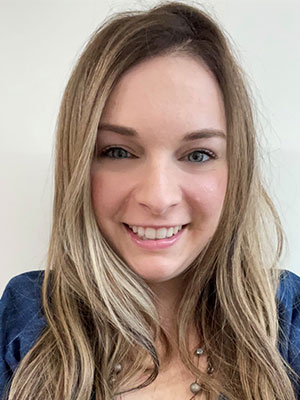 Jessica Barkley wearing a blue top and a beaded necklace, with long light‑brown hair, posed against a plain light background.