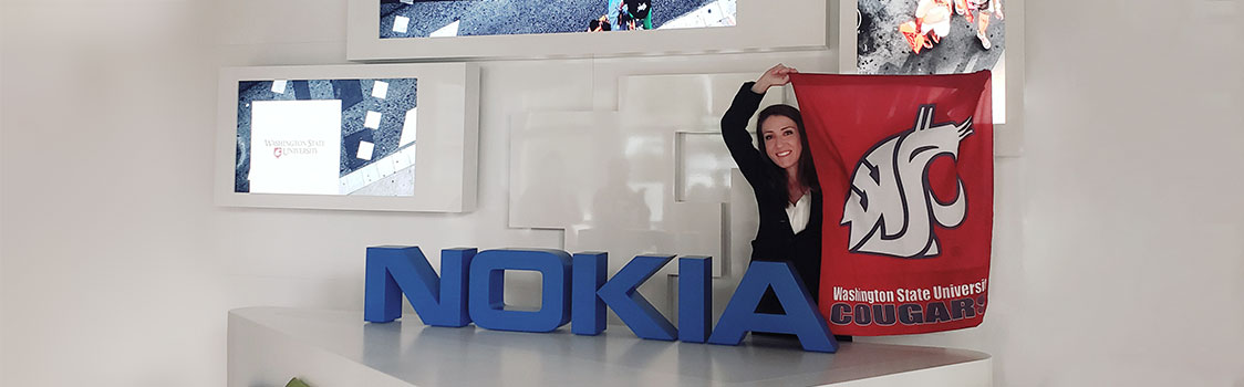 Melanie Wood holding a WSU Cougars flag stands beside a large Nokia sign inside Nokia’s corporate headquarters