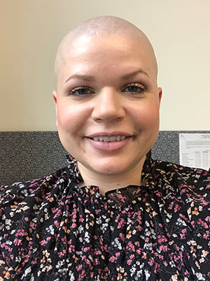 Nicola Lippetti wearing a black top with a pink and white floral pattern, seated indoors with a beige wall and office paneling in the background.